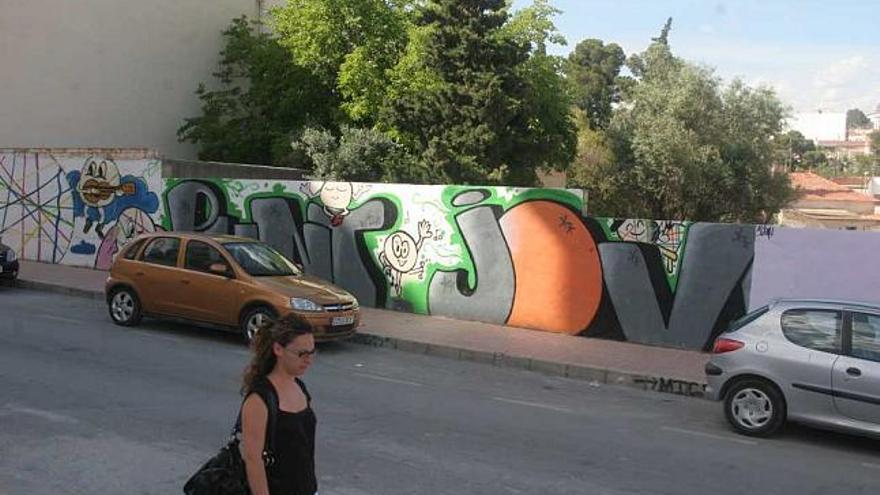 Una joven pasa delante de una pared llena de grafittis en Monóvar.