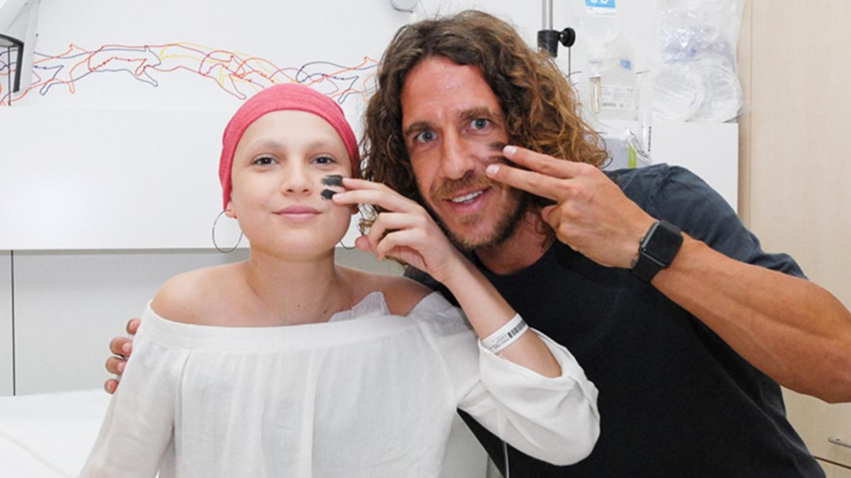 Carles Puyol y una paciente del Hospital de día posan con la cara pintada haciendo el gesto de la campaña del SJD Pediatric Cancer Center Barcelona.