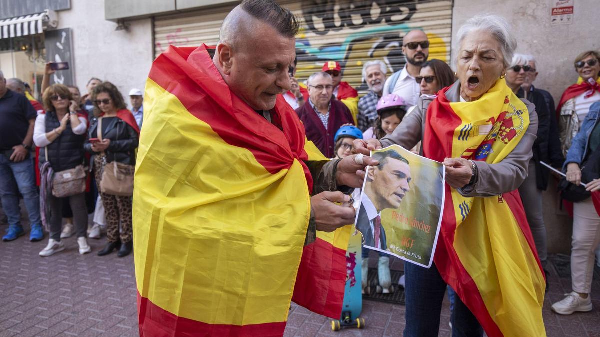 Dos personas tratan de quemar un cartel con la foto de Pedro Sánchez.