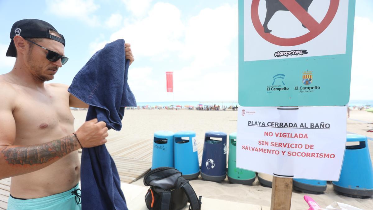 Un cartel que alerta de la falta de socorristas, con la playa al fondo llena con la bandera roja izada en pasado fin de semana