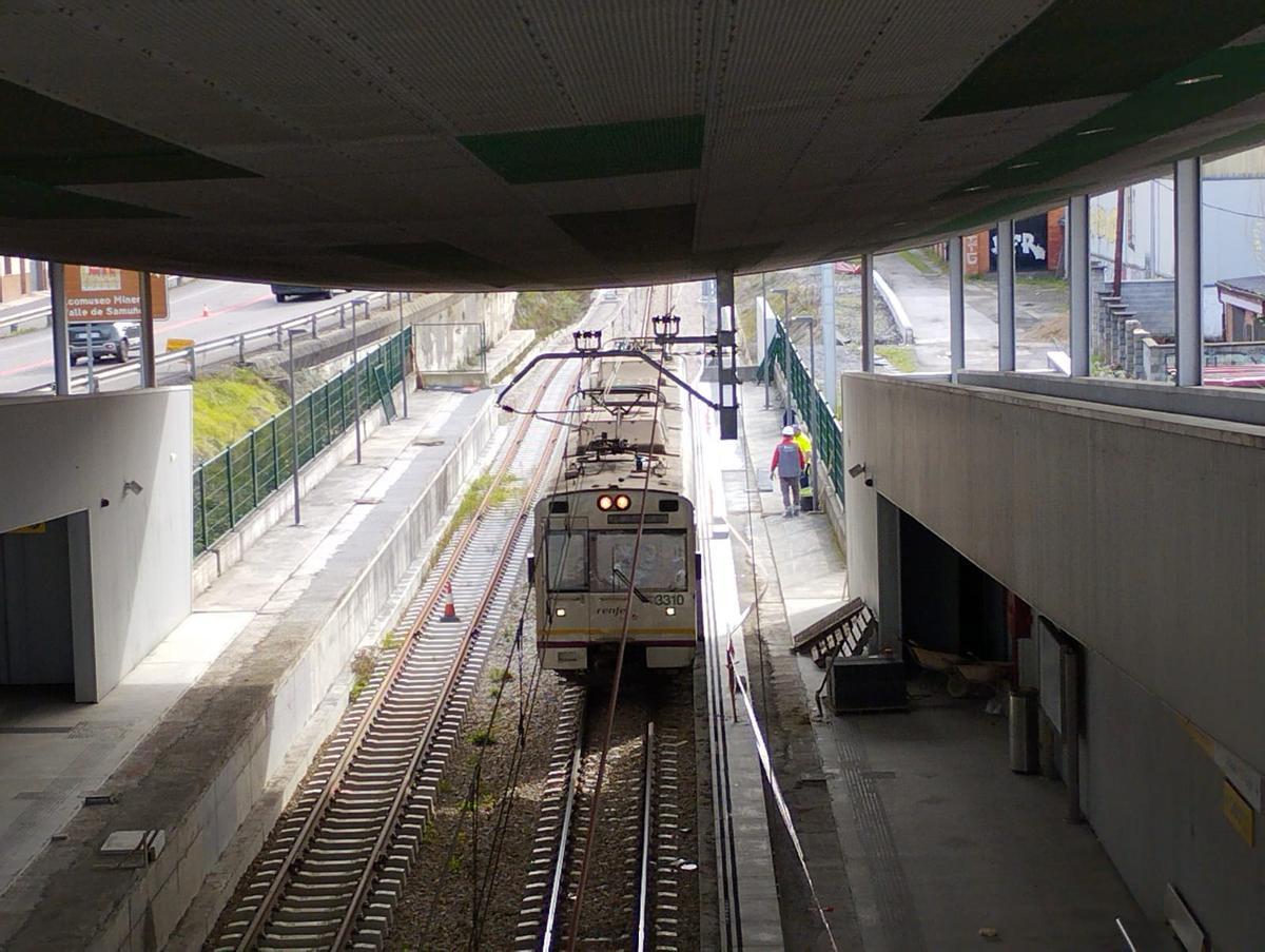 Un tren pasa por la nueva estación de Sama con los operarios trabajando.
