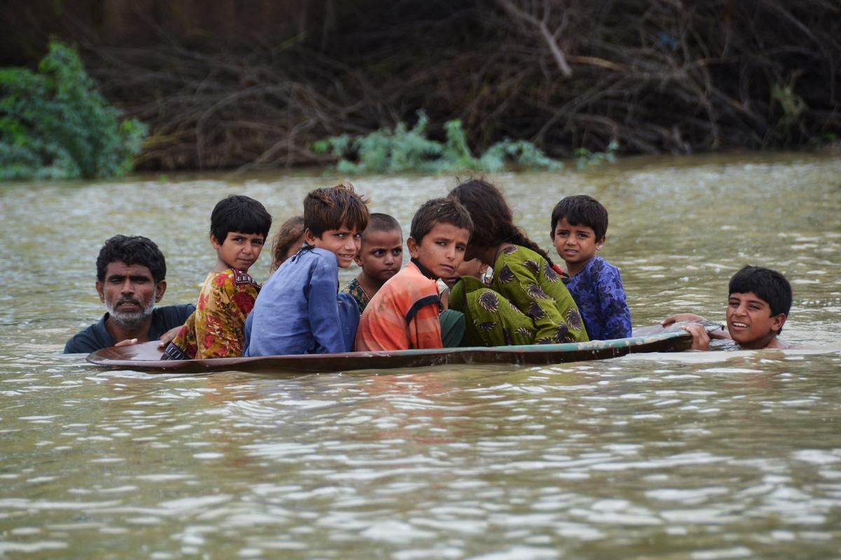 Un hombre y un chico joven usan un disco de una antena de satélite para trasladar a un grupo de niños en el área inundada tras intensas lluvias causadas por los monzones en el distrito de Jaffarabad, en la provincia de Balochistan, en Pakistán, el 26 de agosto del 2022.