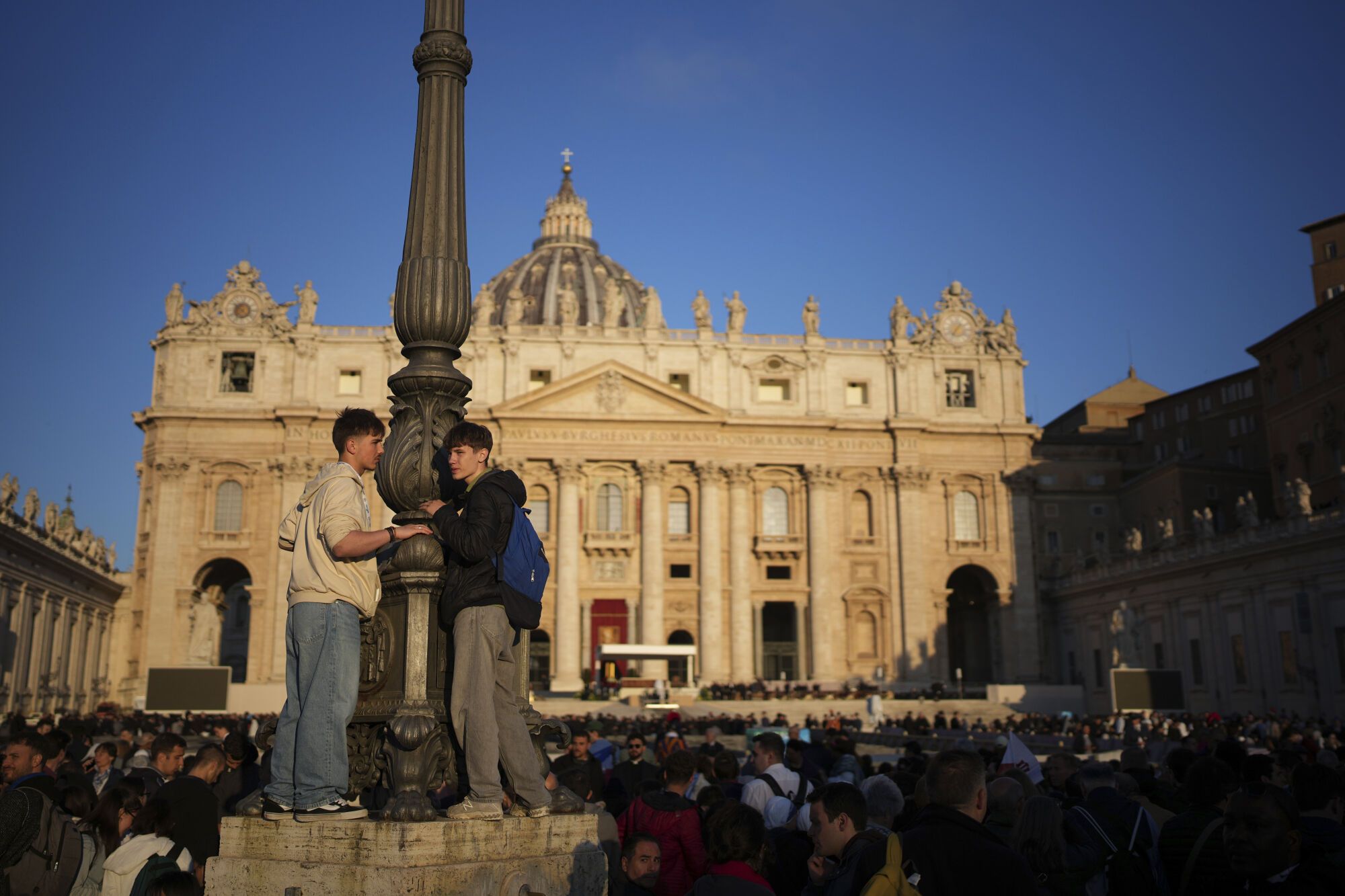 Faithful stand in a lamppost as they wait for the funeral of Pope Francis to begin in St. Peter's Square, at the Vatican, Saturday, April 26, 2025. (AP Photo/Emilio Morenatti)