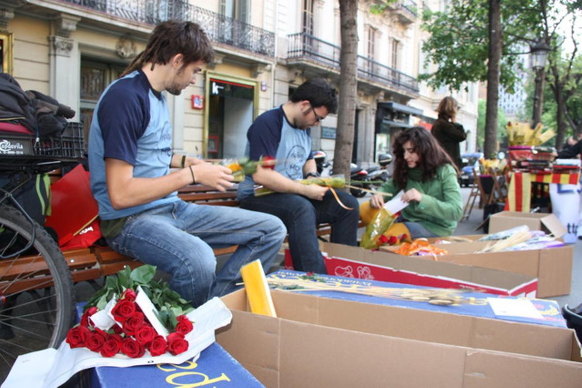 Unos jóvenes preparan su puesto de rosas, a primera hora de la mañana en la Rambla de Catalunya.