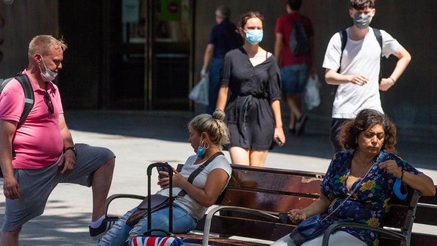 Varias personas descansan en un banco en las Ramblas..