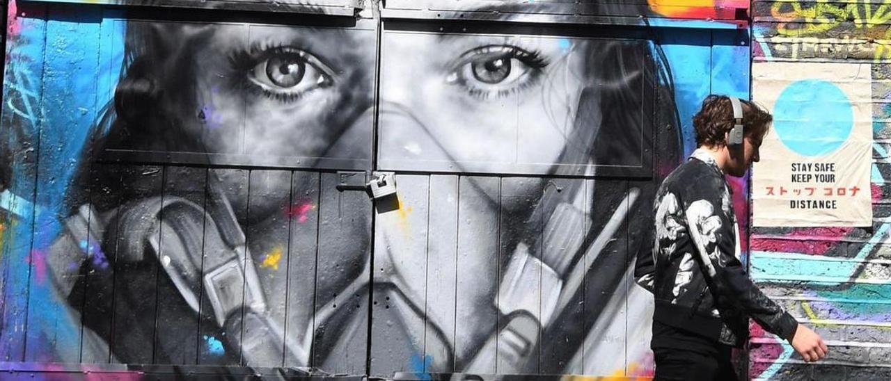 Un joven pasea frente a un grafiti de una mujer con una mascarilla. |