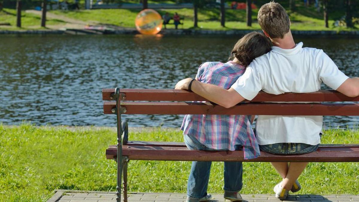 Una pareja de adolescentes, en el banco de un parque.