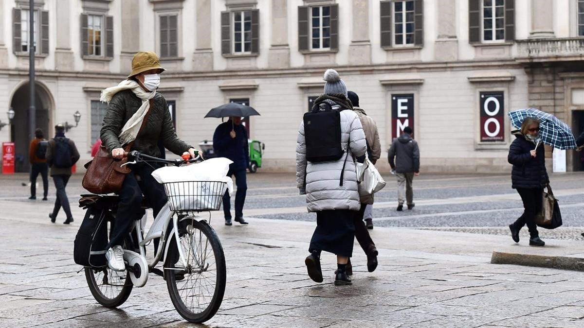 Una mujer pasea en bici, con mascarilla, por Milán.