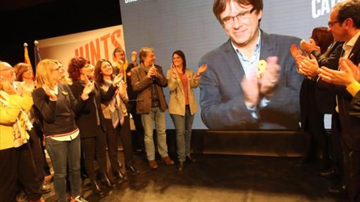 El escenario del mitin de JxCat, con Puigdemont en la pantalla y su esposa aplaudiendo (tercera por la izqda.).