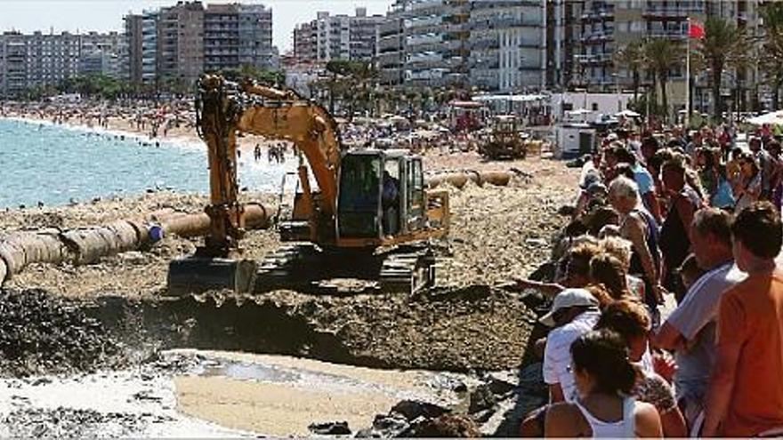 Curiosos seguint les obres i banyistes a la part oberta de la platja.