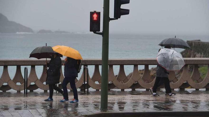 Varias personas se resguardan de la lluvia en el paseo marítimo de A Coruña.