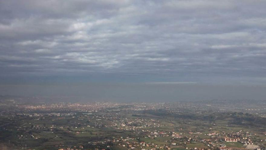 Vista de Gijón desde el Pico El Sol, con el poblado de La Camocha en primer término y con una capa de contaminación sobre la ciudad, bajo las nubes.