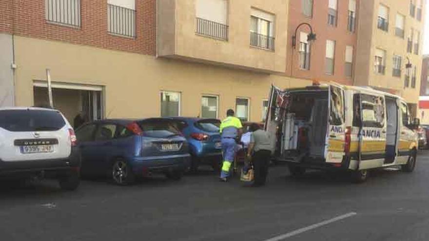 El conductor de una ambulancia lleva a un paciente en silla de ruedas al centro de hemodiálisis entre numerosos coches estacionados.