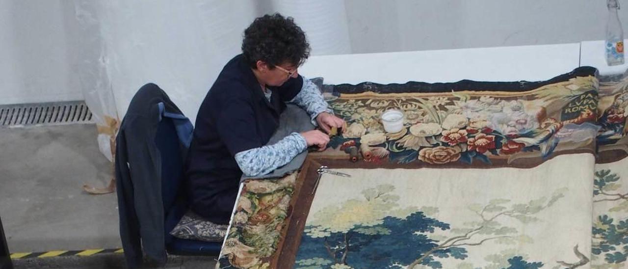 Las restauradoras Manuela Pérez y Conchi Yubero trabajan sobre una alfombra que reproduce la historia de Rómulo y Remo.