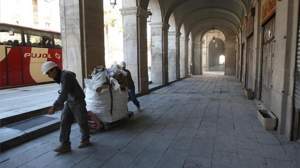 Dos obreros retiran una bolsa llena de escombros de una de las fincas en rehabilitación del entorno de los porches de Xifré.