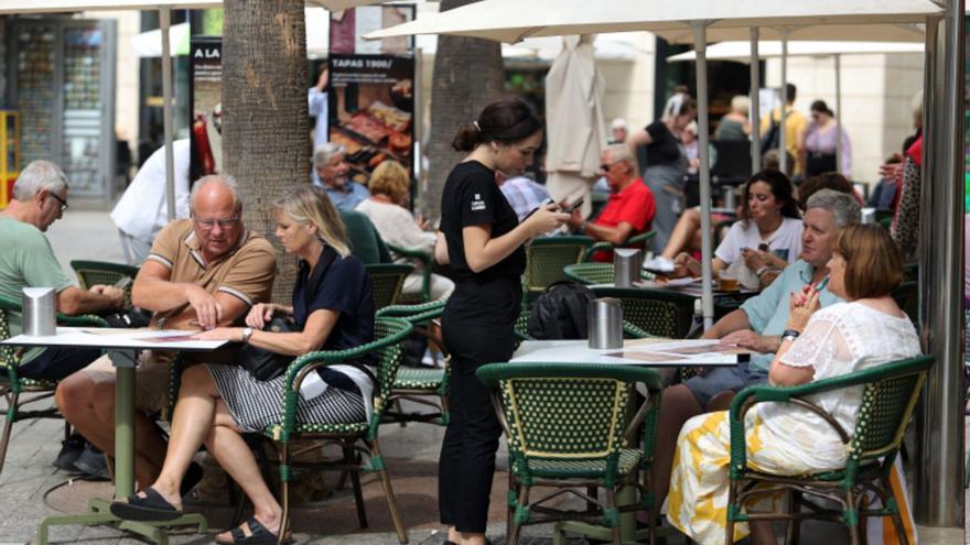 Una trabajadora del sector de la hostelería atiende a unos clientes en Málaga. | ÁLEX ZEA