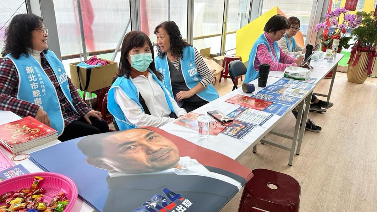 Un grupo de mujeres trabajando en la sede electoral del Kuomintang, con un cartel de su candidato, Hou Yu-ih sobre la mesa.