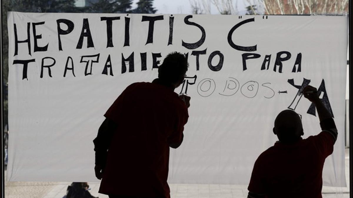 Dos hombres pintan un cartel reclamando acceso universal al nuevo tratamiento de la hepatitis C, en Navarra.