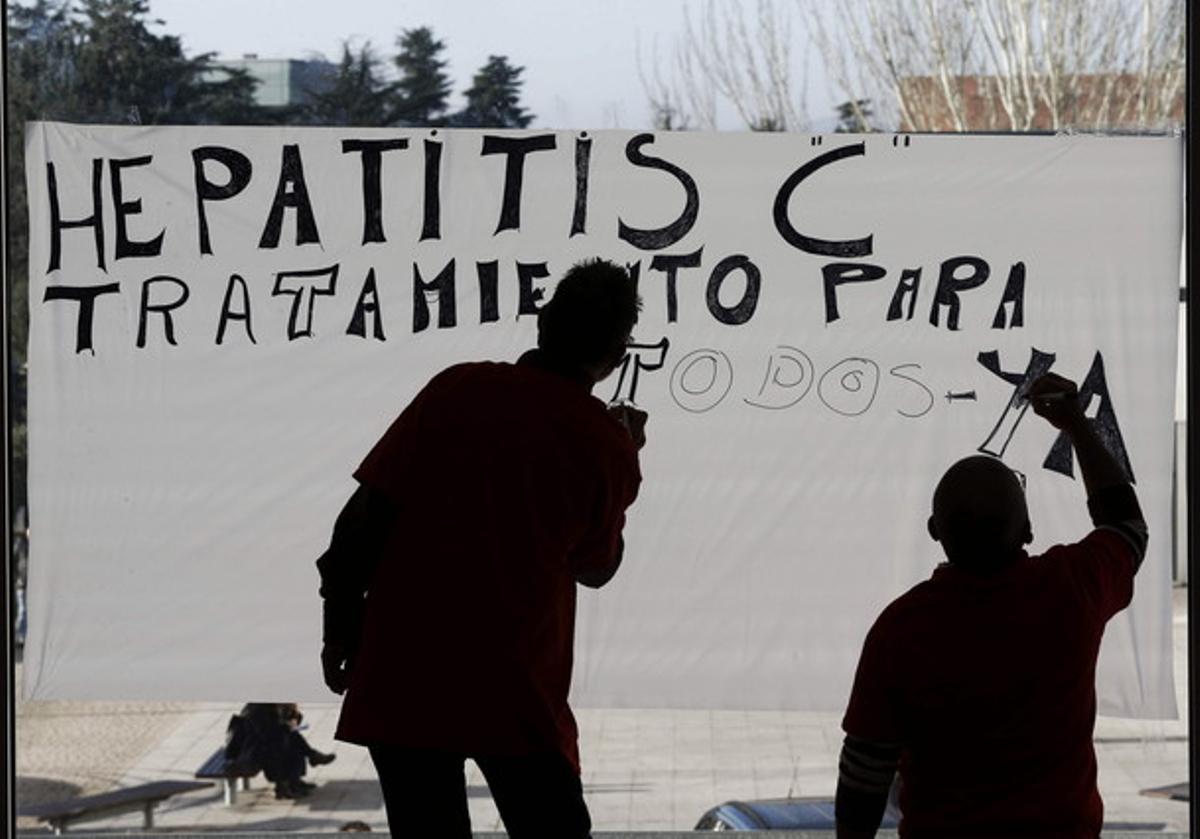 Dos homes pinten un cartell reclamant accés universal al nou tractament de l’hepatitis C, a Navarra.
