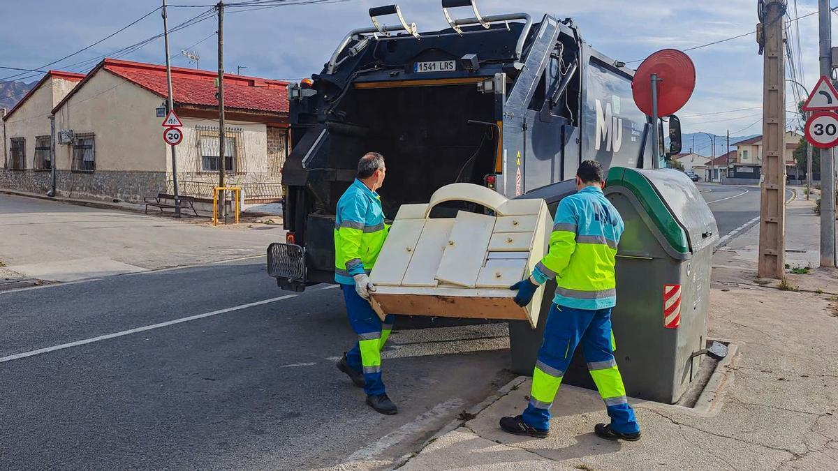 Dos operarios municipales del servicio de recogida de enseres retiran un mueble.