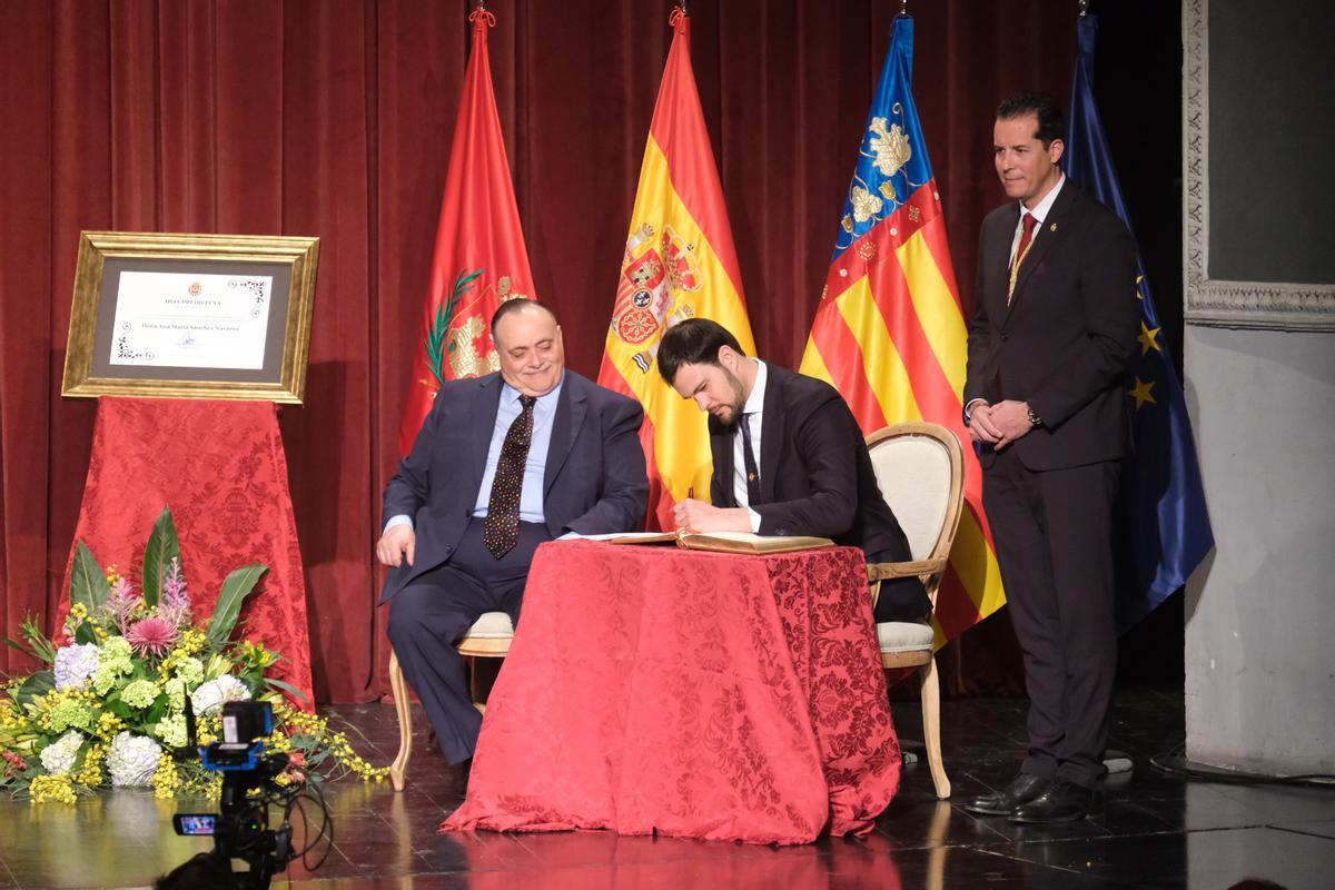 El alcalde de Elda, de pie, mientras el hijo de la soprano firma en el Libro de Honor del Ayuntamiento.