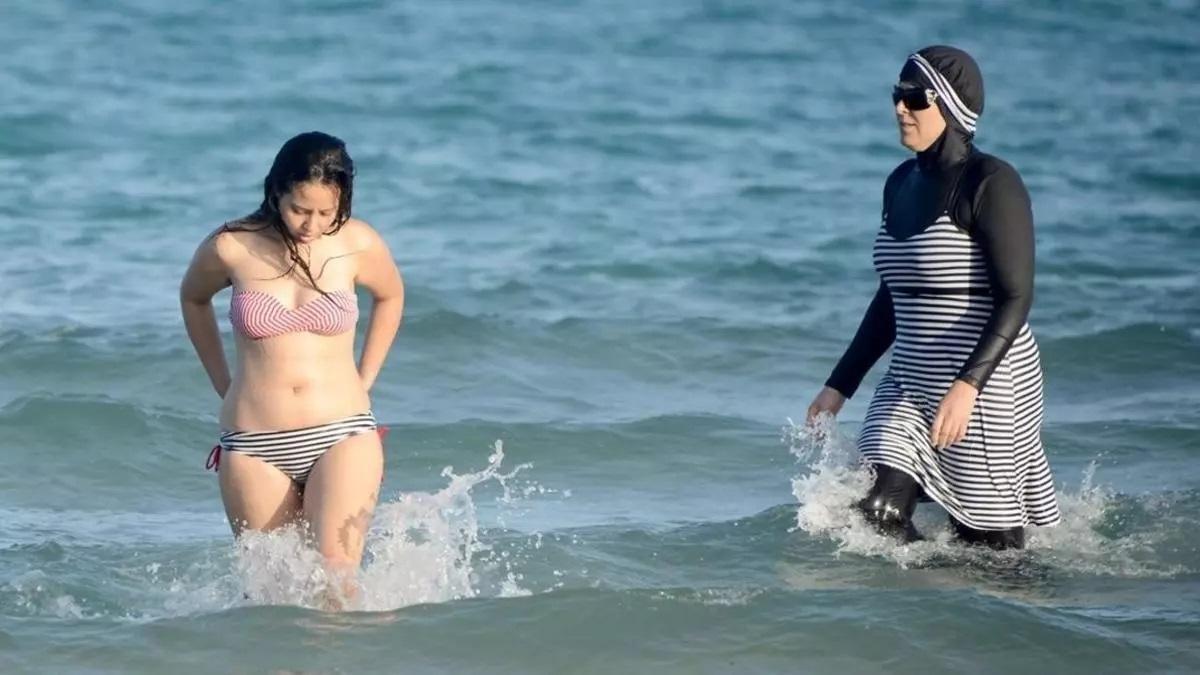 Una mujer se baña con un burkini frente a otra, que lo hace en bikini.