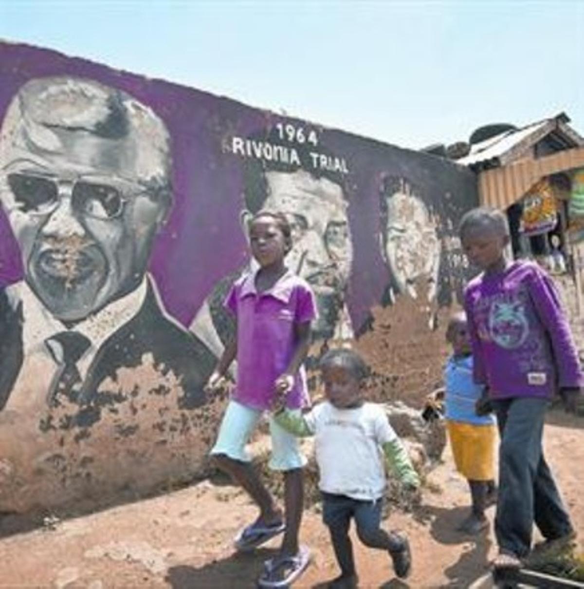 Uns nens caminen davant d’un mural de Mandela, ahir a Soweto.