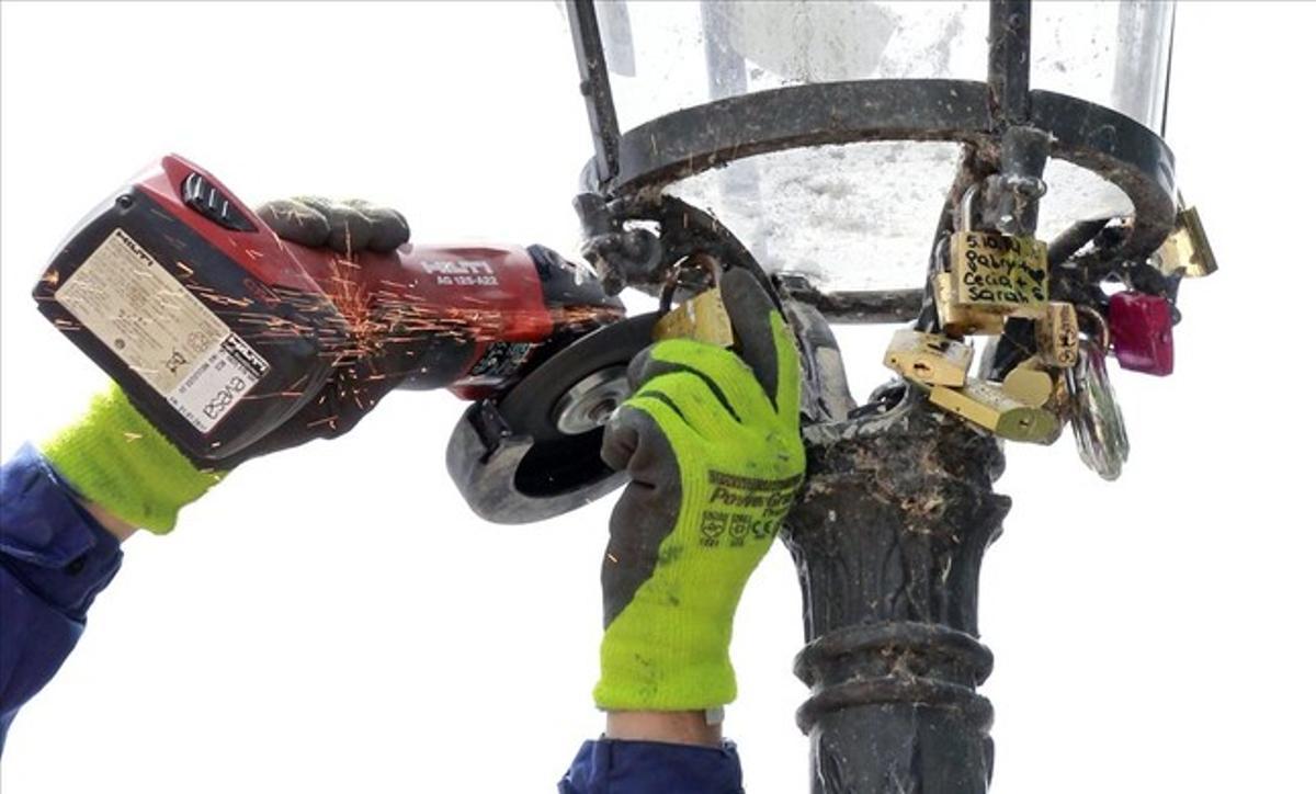 Un operari retira candaus de l’estructura d’un fanal pròxim al pont de les Arts de París. Els enamorats, a més de penjar candaus a les baranes del pont, també n’havien posat als fanals.