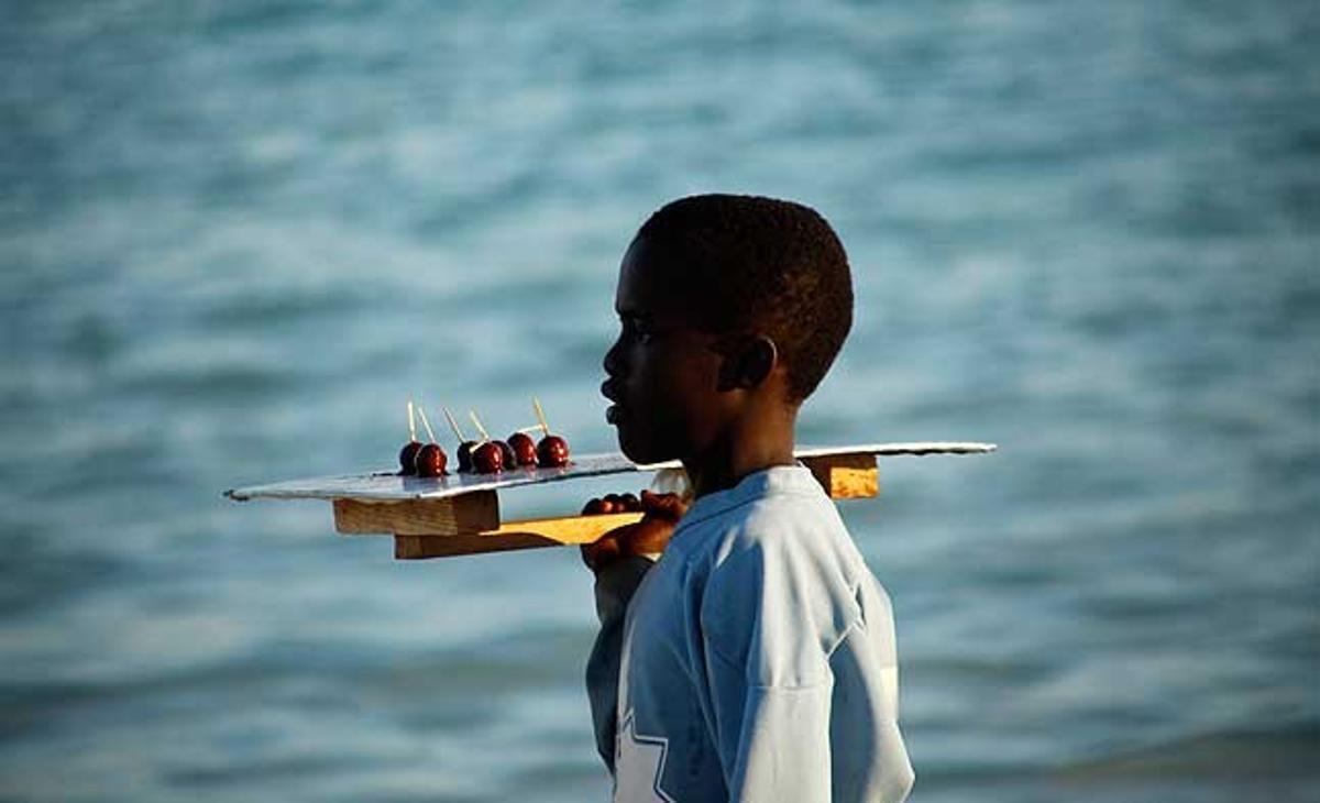 Un nen porta una safata de dolços casolans per vendre, mentre busca clients a la platja pública de Boca Chica, a la República Dominicana.