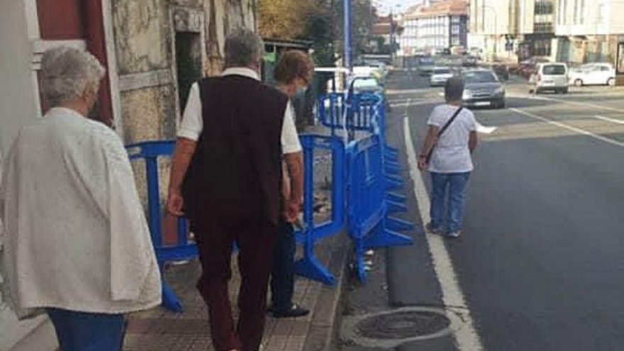 Transeúntes bajan de la acera junto a las vallas ante la casa. |  // L.O.