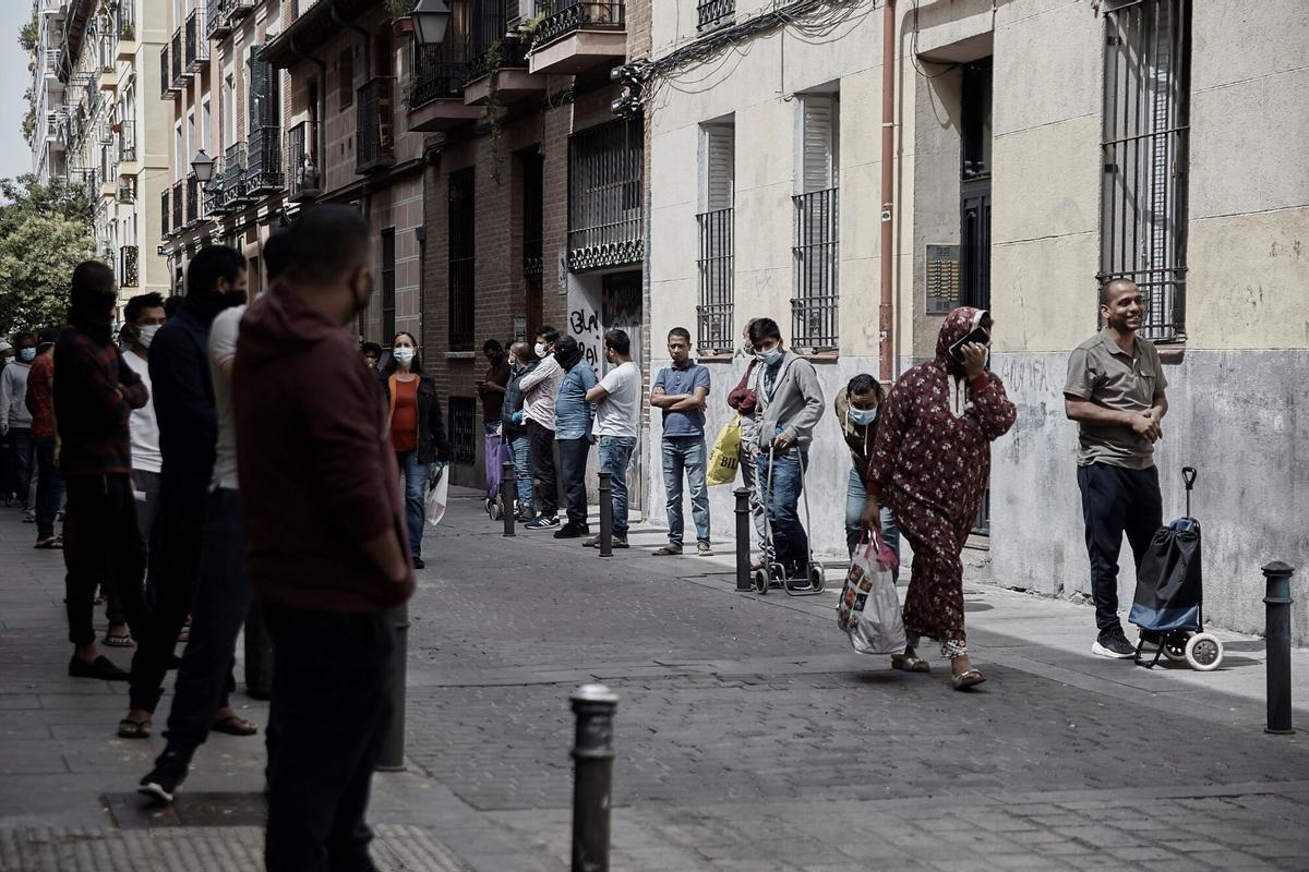 Varias personas hacen cola a la espera del reparto de alimentos por parte de la asociación de Valiente Bangla en el barrio de Lavapiés.