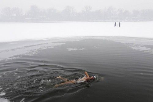 A person swims as people walk on the partially frozen Houhai Lake during winter in central Beijing
