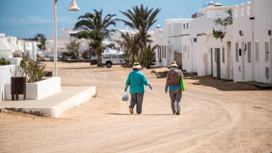 Dos mujeres con el típico sombrero graciosero caminan por Caleta de Sebo.