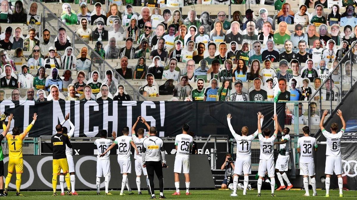 Los jugadores del Borussia de Mönchengladbach se dirigen a las gradas del estadio, ocupadas con fotografías de sus aficionados.