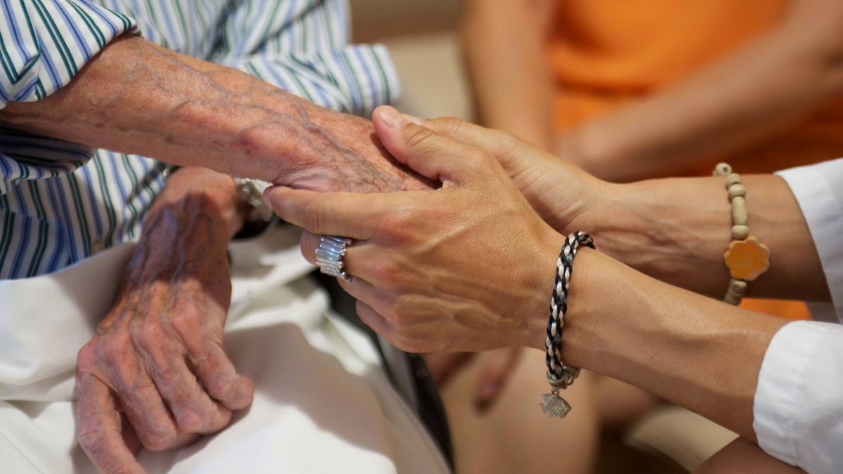 Una sanitaria toma la mano de una anciana.