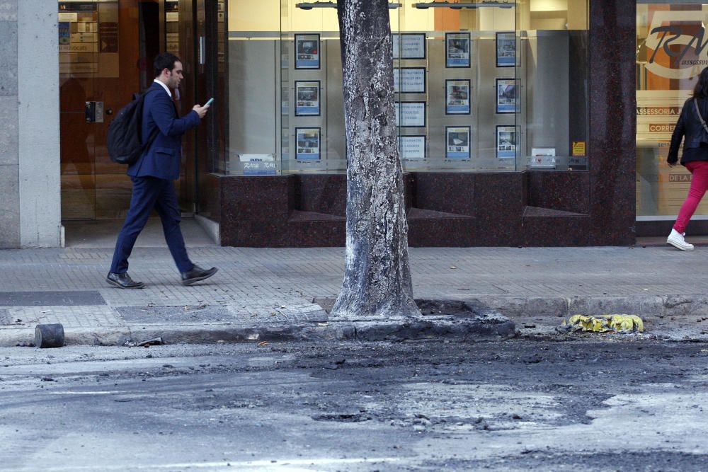 Carrers amb restes de mobiliari urbà cremat, contenidors per terra i treballadors de la brigada treballant