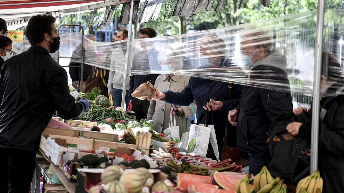 Un vendedor de frutas y verduras atiende a los clientes detrás de una protección de plástico en el mercado Place des Fetes en París.