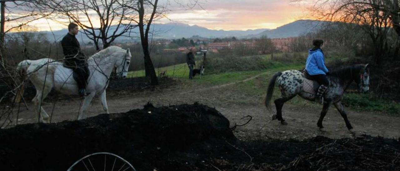 Dos jóvenes a caballo atraviesan una zona afectada por las llamas, con La Fresneda al fondo.