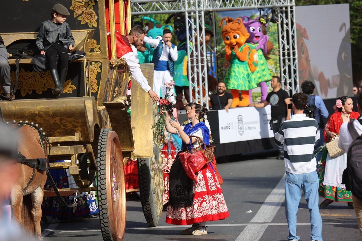 Un joven en una carroza recoge las flores que le da una chica.