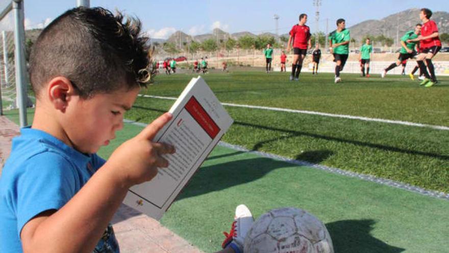 Un niño lee un libro tendido en el cesped de uno de los campos de la Sismat en Elda .