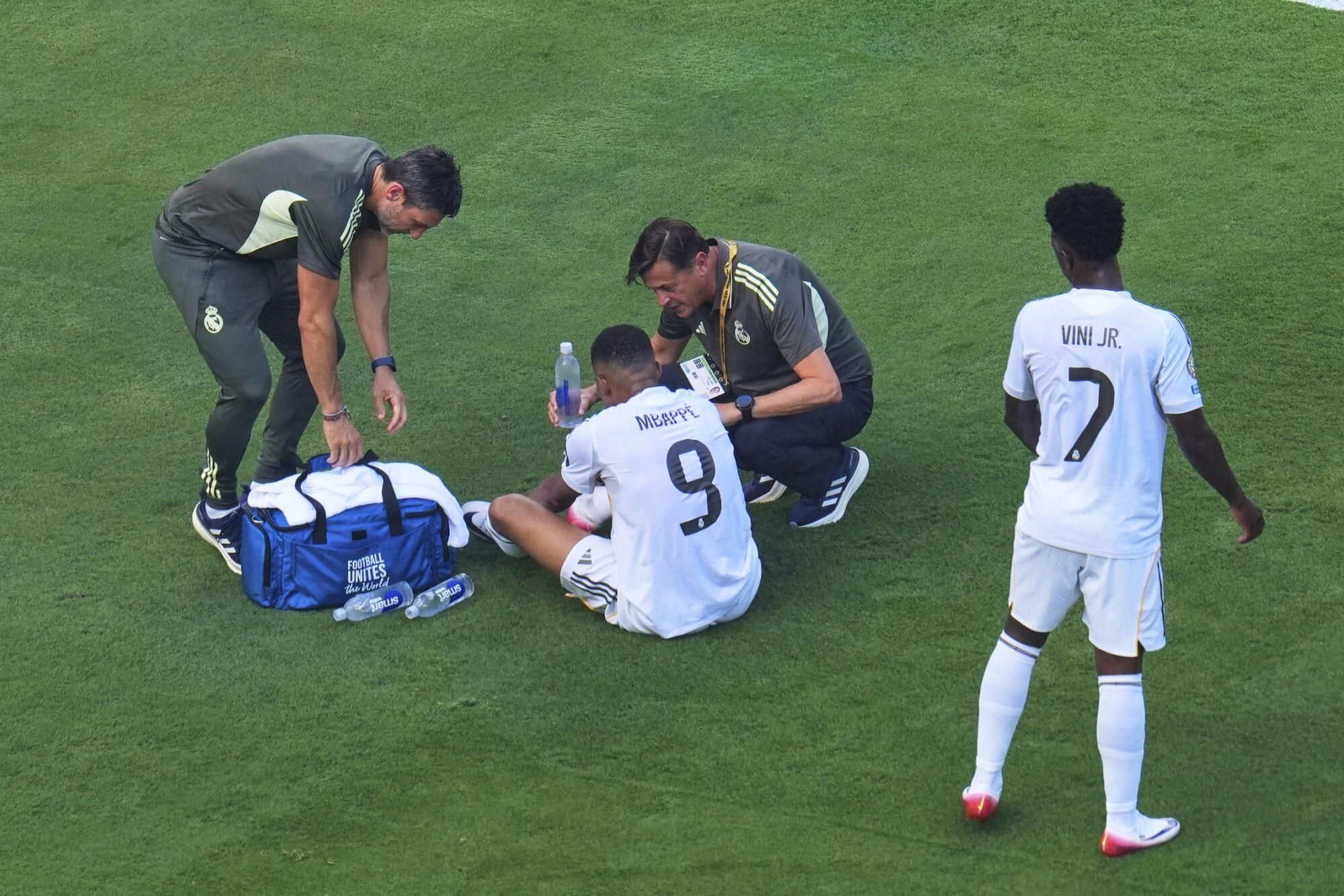 Real Madrid's Kylian Mbappe (9) is checked out by team staff after a play against Paris Saint-Germain's Joao Neves (87) as Vinicius Junior (7) looks on during the Club World Cup semifinal soccer match between PSG and Real Madrid in East Rutherford, N.J., Wednesday, July 9, 2025. (AP Photo/Pamela Smith)