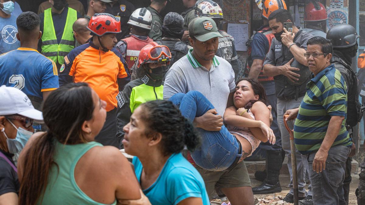 Un hombre carga a una mujer en la zona donde se derrumbó un edificio de tres pisos este lunes, en el barrio Unión de Petare en Caracas (Venezuela).