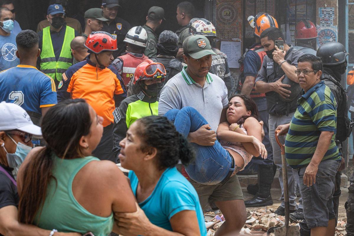 Un hombre carga a una mujer en la zona donde se derrumbó un edificio de tres pisos este lunes, en el barrio Unión de Petare en Caracas (Venezuela).