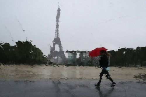 Rain drops on a car window distort the Eiffel Tower as a woman takes shelter under an umbrella during a rain shower in Paris