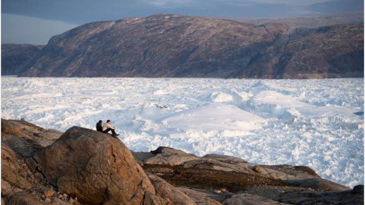 Los investigadores se sientan en la cima de una roca con vista al glaciar Helheim, en Groenlandia.