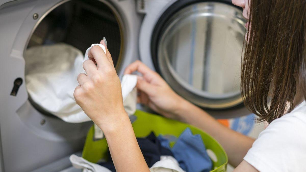 Una mujer mete una prenda blanca en la lavadora.