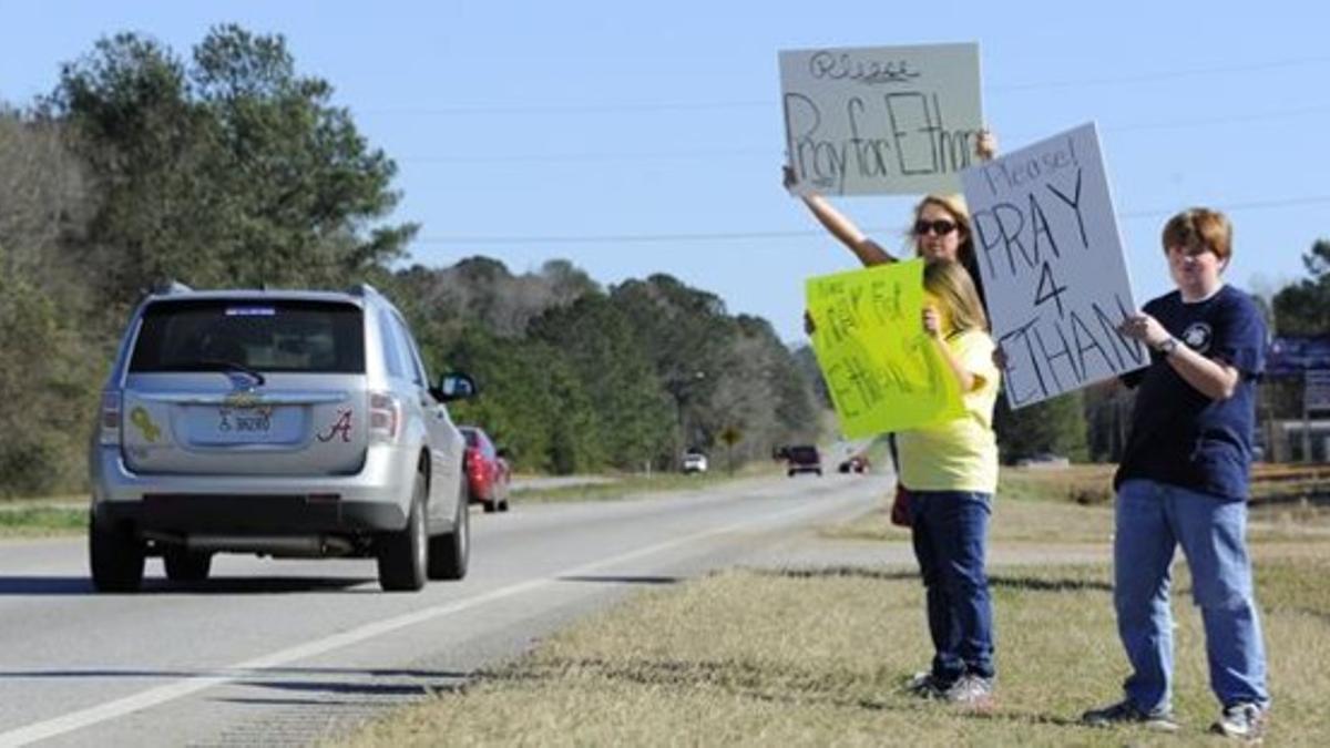 Una madre y sus dos hijos muestran carteles rogando a los automovilistas que rezaran por Ethan, en Midland City (Alabama).