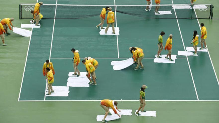 Voluntarios tratan de secar la pista de tenis con toallas.