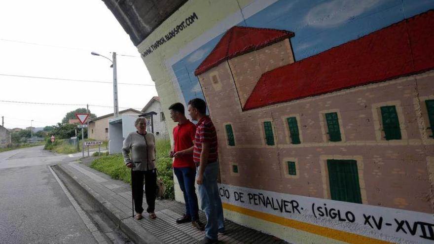 Jorge Suárez e Iván Fernández charlan con una vecina frente a uno de los murales de José &quot;Poch&quot;, en el túnel decorado de Trasona.