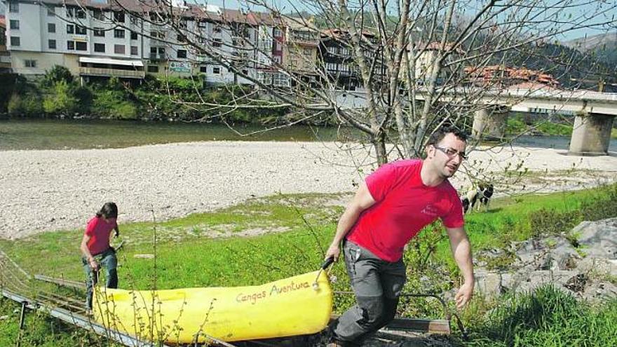 David García, «Fifu», y Daniel Cue sacan una canoa del Sella, con el puente a la derecha y Arriondas al fondo. / jesús farpón